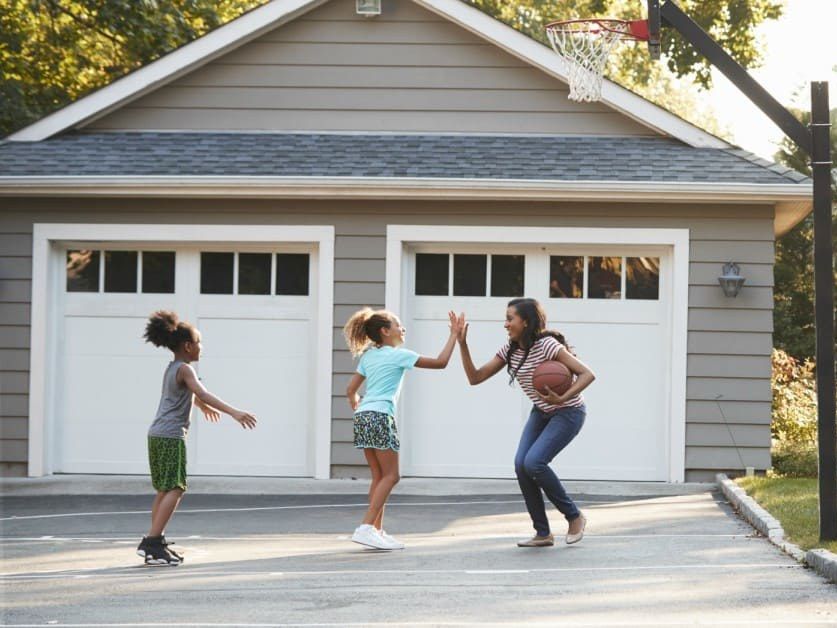 A nanny playing basketball with two children in a driveway